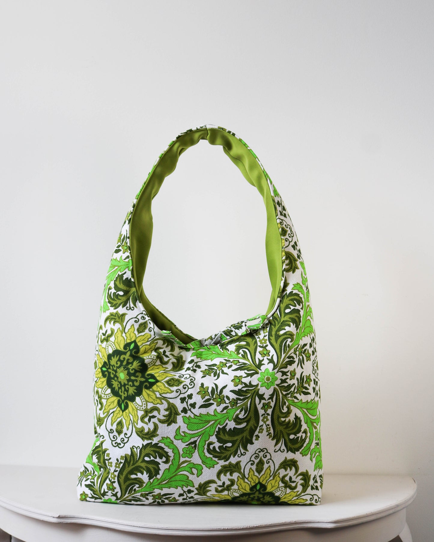 Green floral patterned handbag on a white surface with a white background