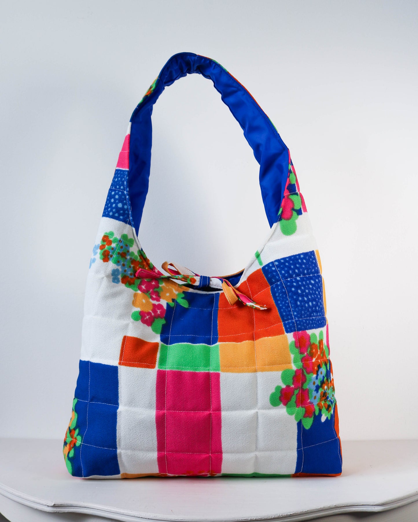Colorful quilted handbag with floral accents on a white background