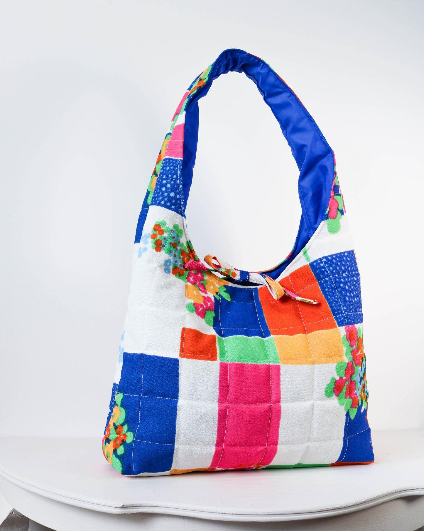 Colorful quilted handbag with floral accents on a white background