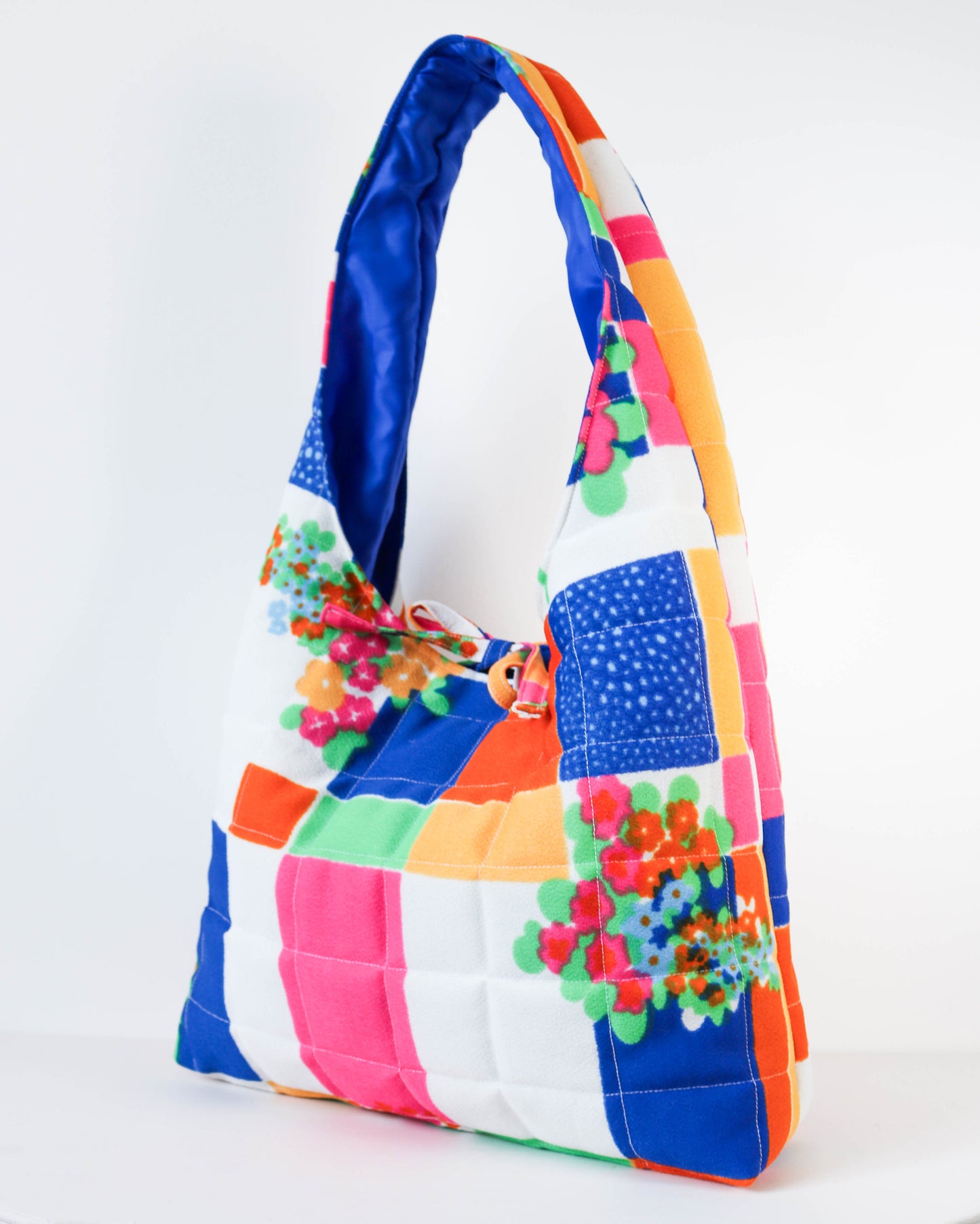 Colorful quilted handbag with floral accents on a white background