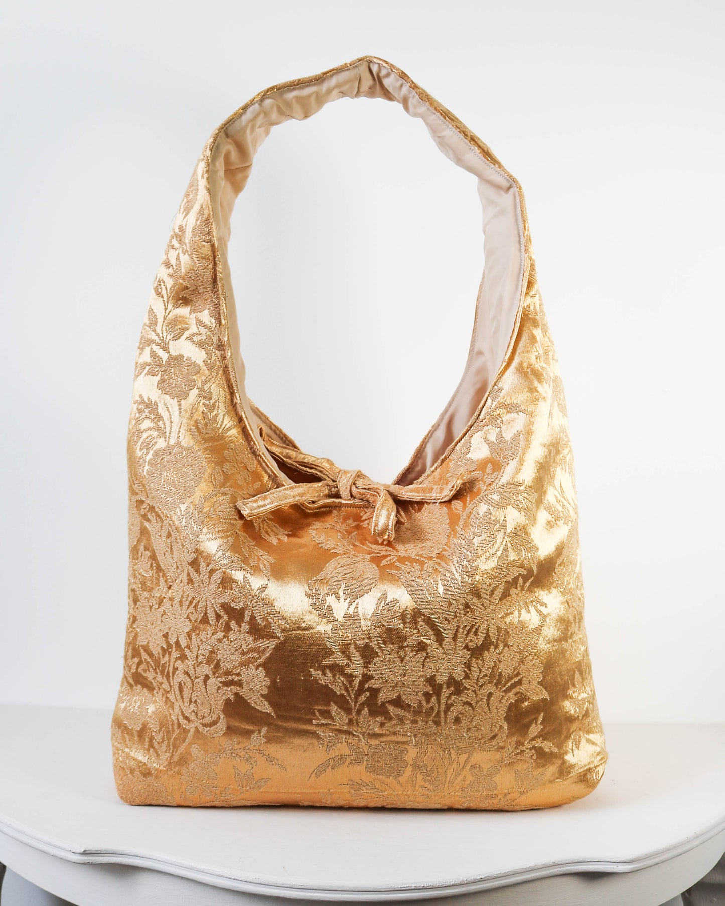Gold floral patterned handbag on a white surface with a white background