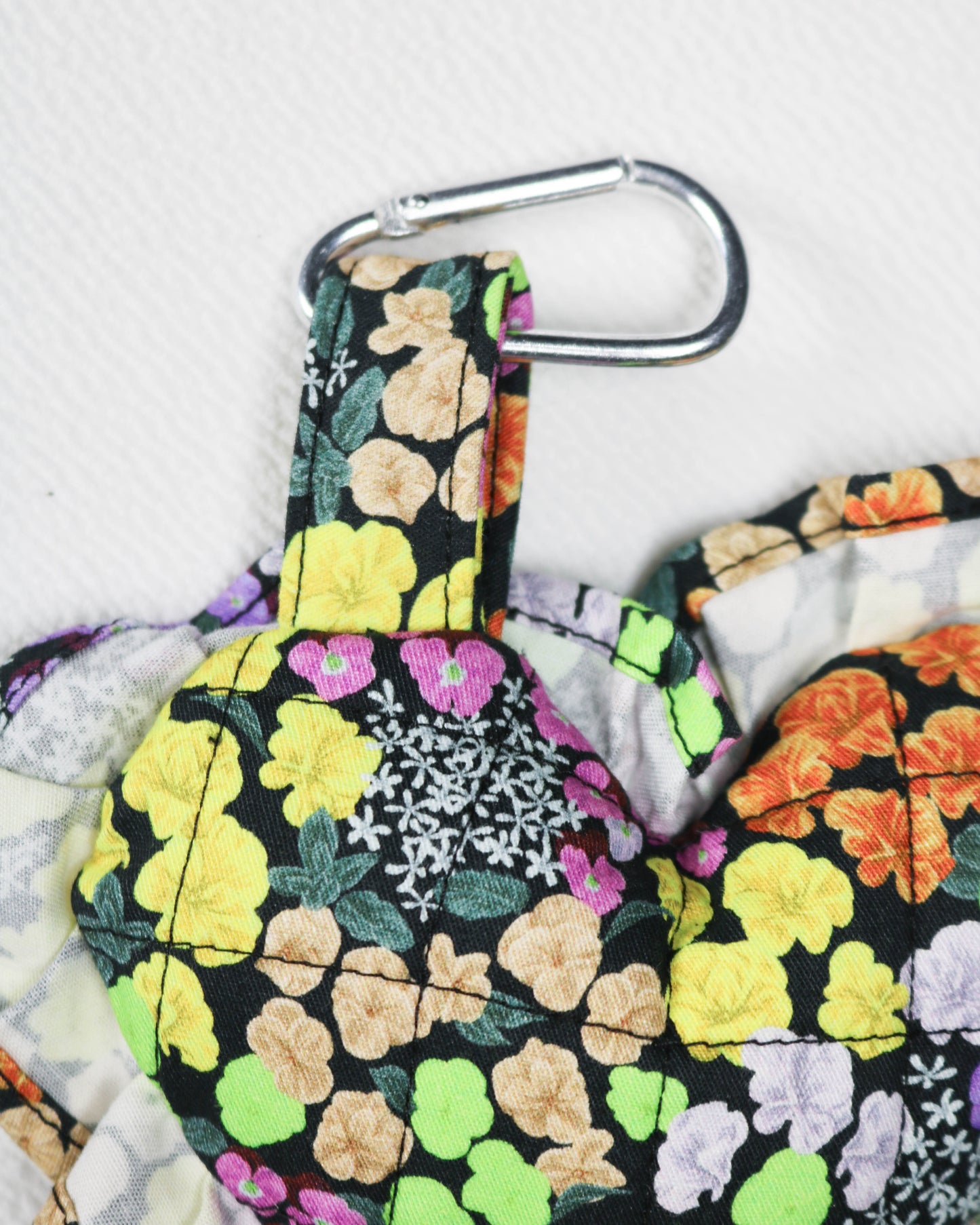 Floral-patterned bag charm with a carabiner clip on a light gray background