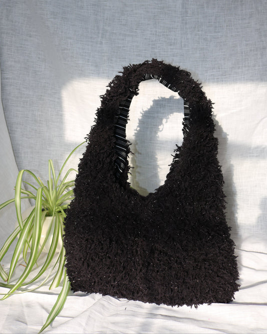 Black textured handbag on a light gray surface with a plant in the corner