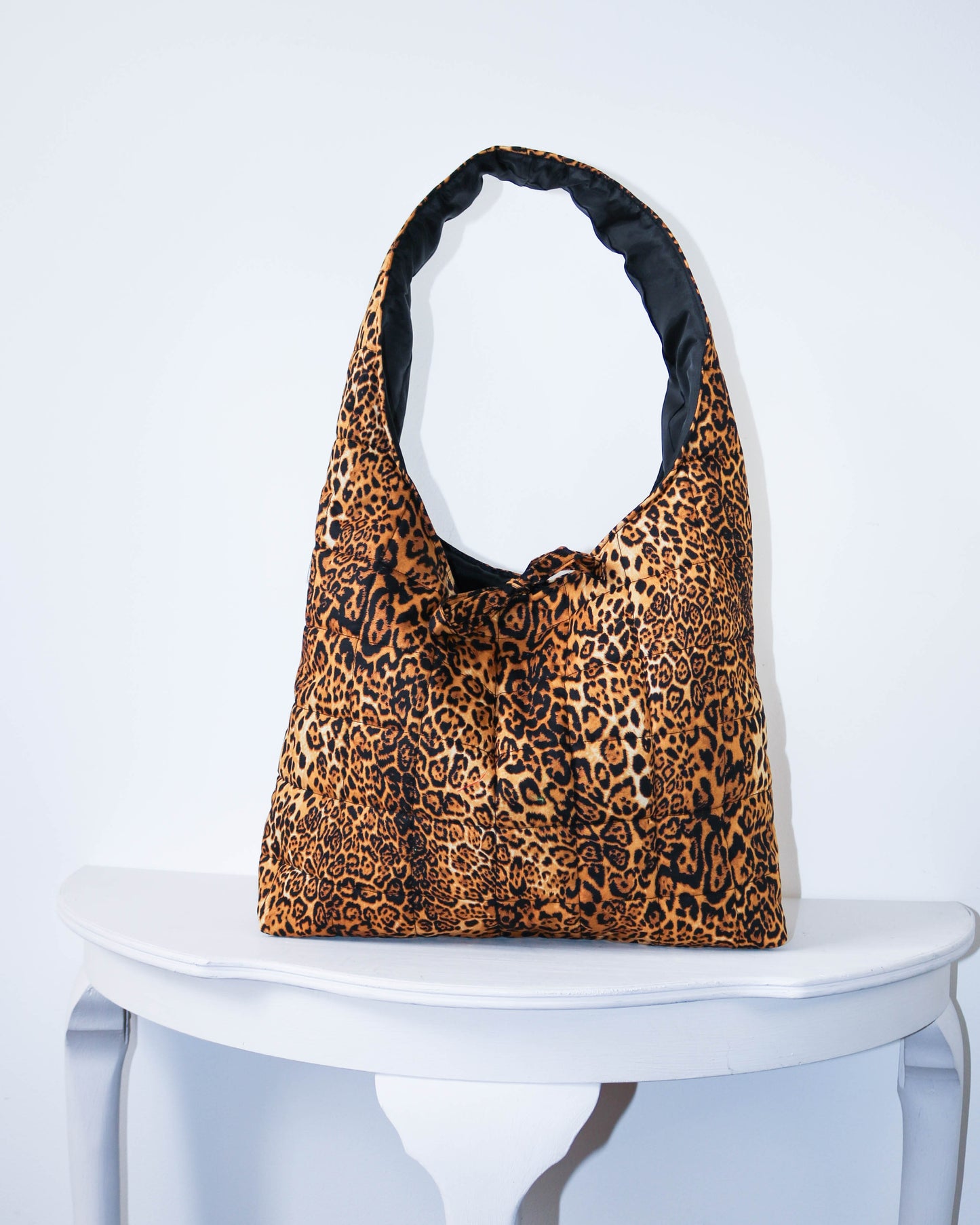 Leopard print bag on a white pedestal against a light gray background