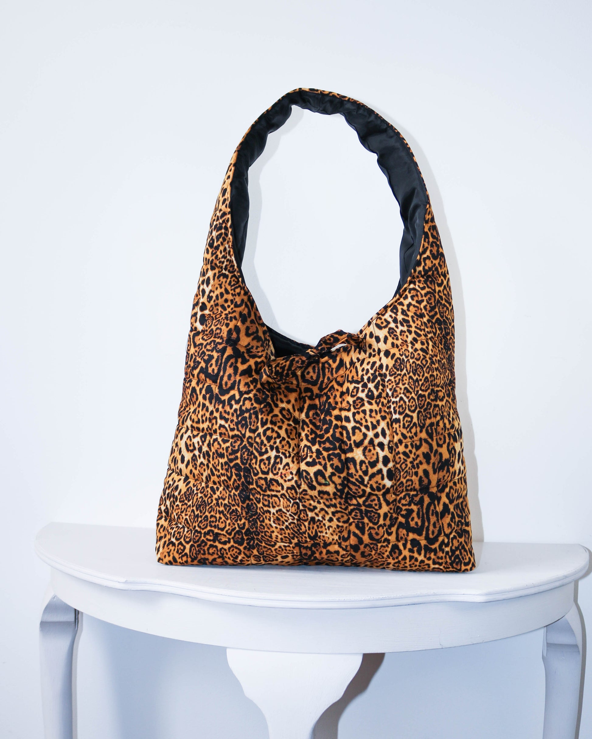 Leopard print bag on a white pedestal against a light gray background