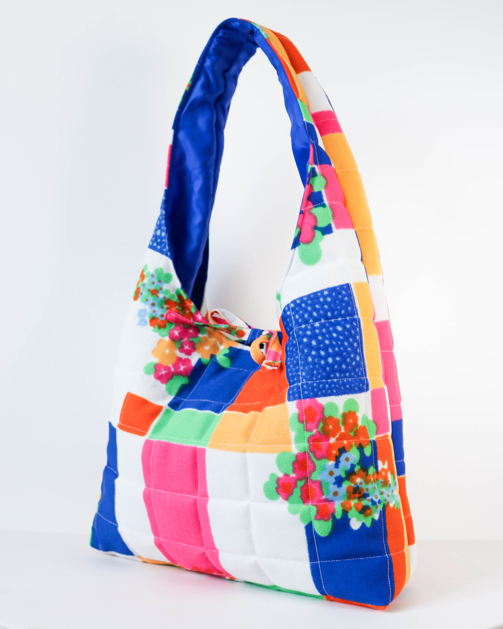 Colorful quilted handbag with floral accents on a white background