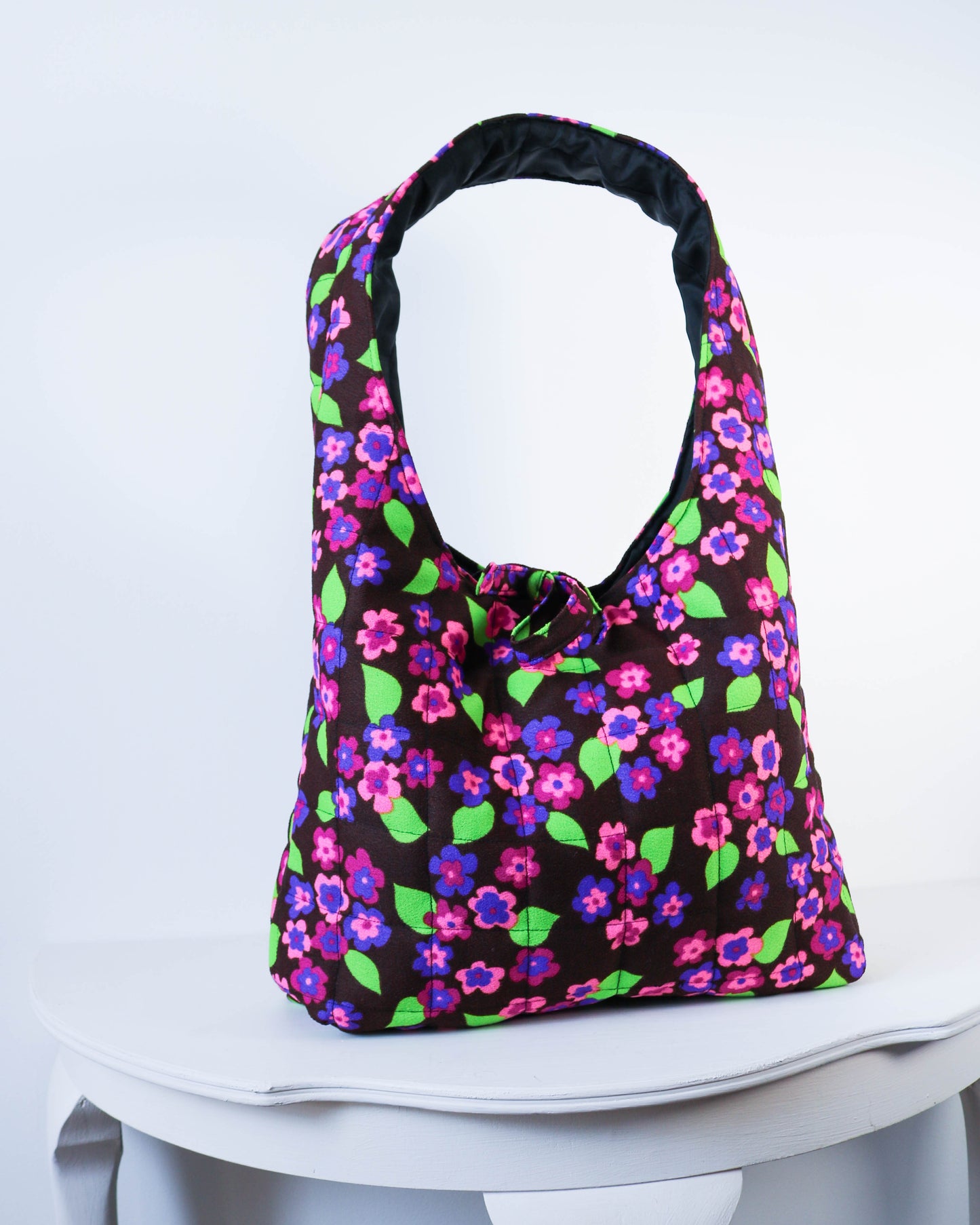 Floral patterned bag on a white stool with a white background