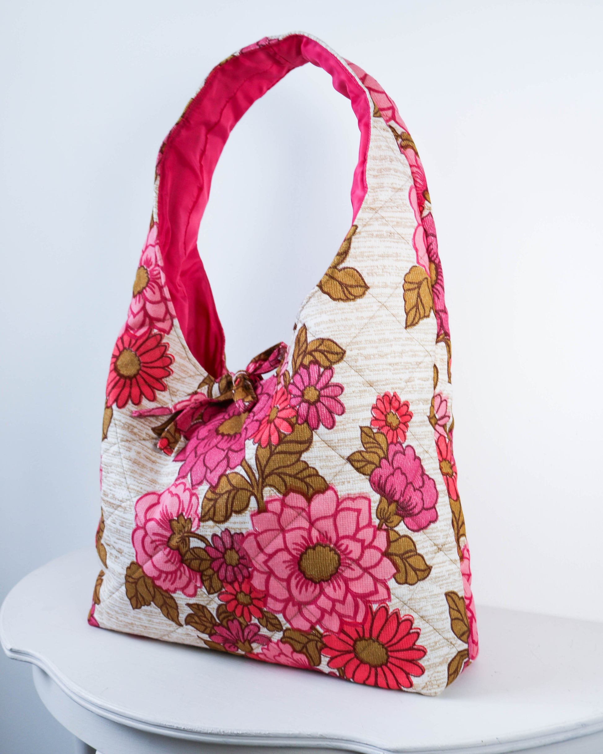 Floral patterned handbag with pink handle on a white surface