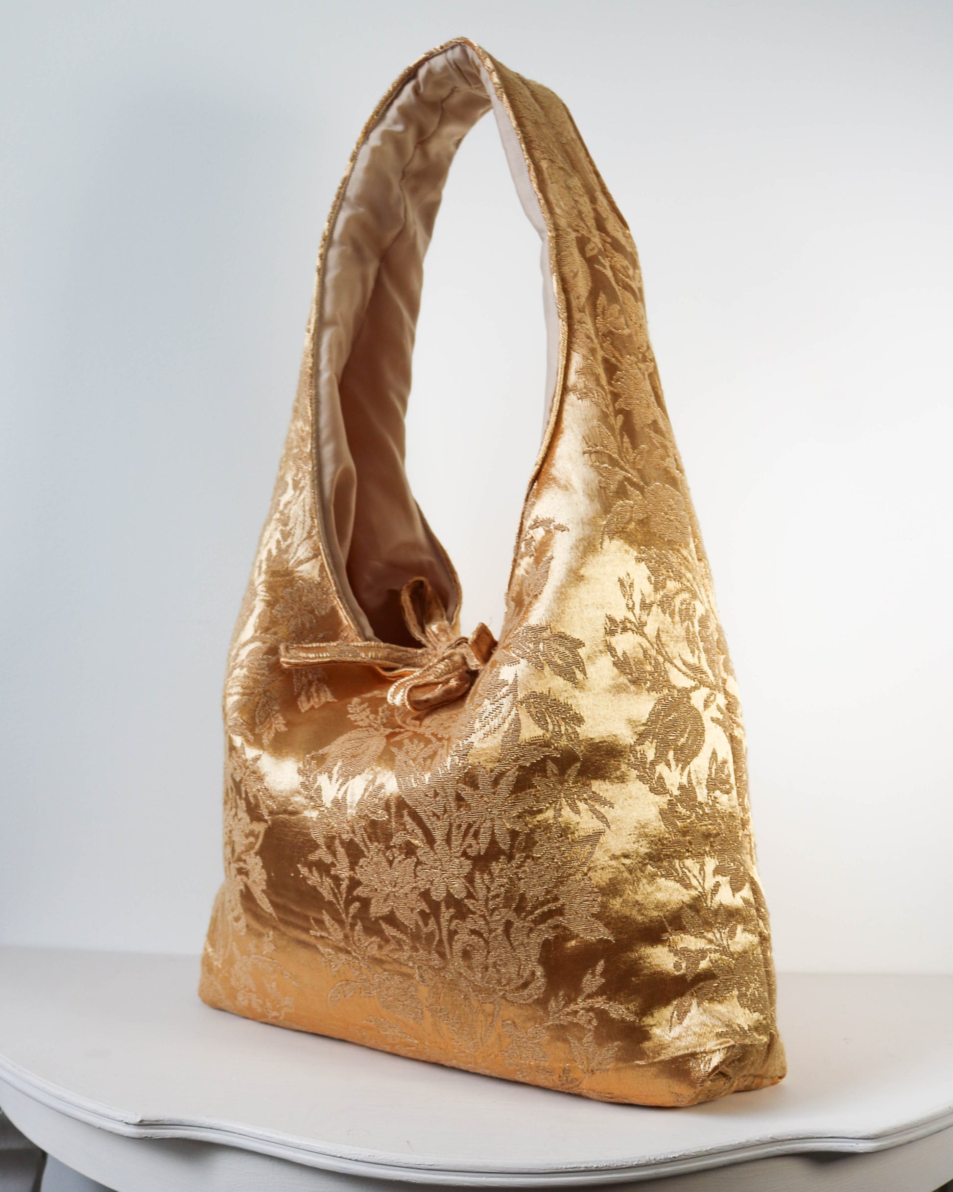 Gold floral patterned handbag on a white surface with a white background