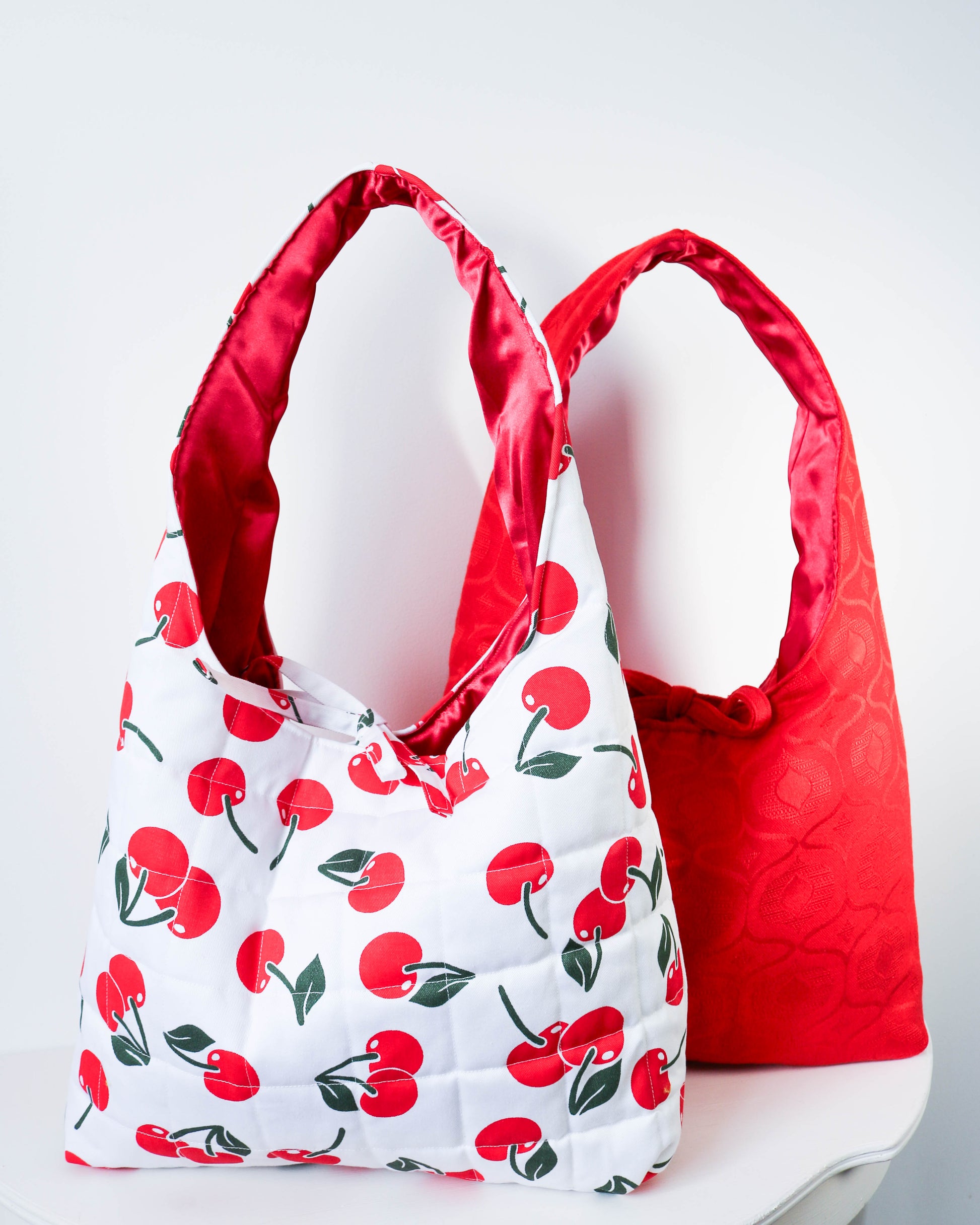 Two bags, one with cherry pattern and the other red, on a white background