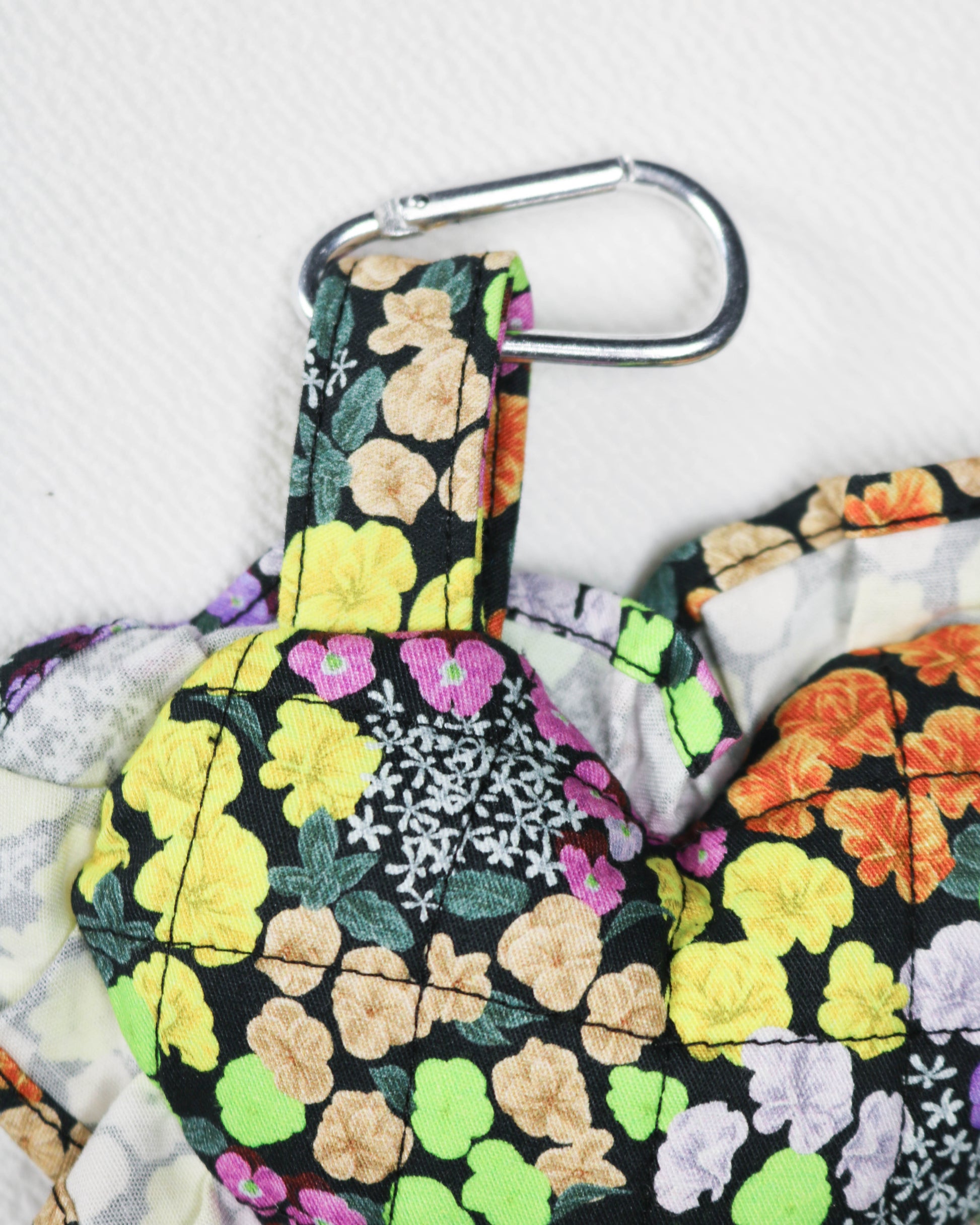 Floral-patterned bag charm with a carabiner clip on a light gray background