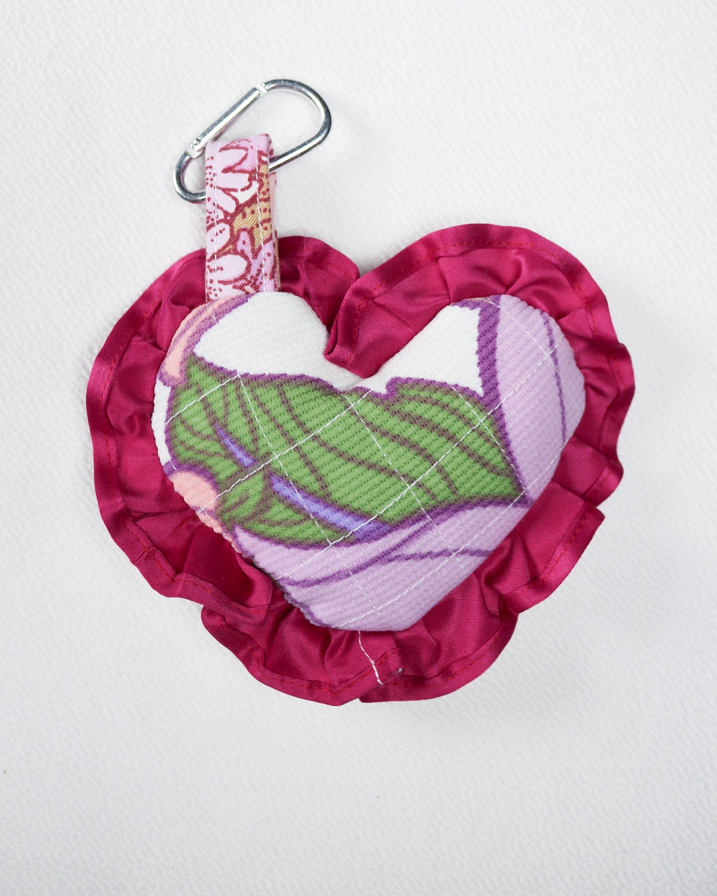 Pink fabric heart with green leaf design and floral strap on a white background