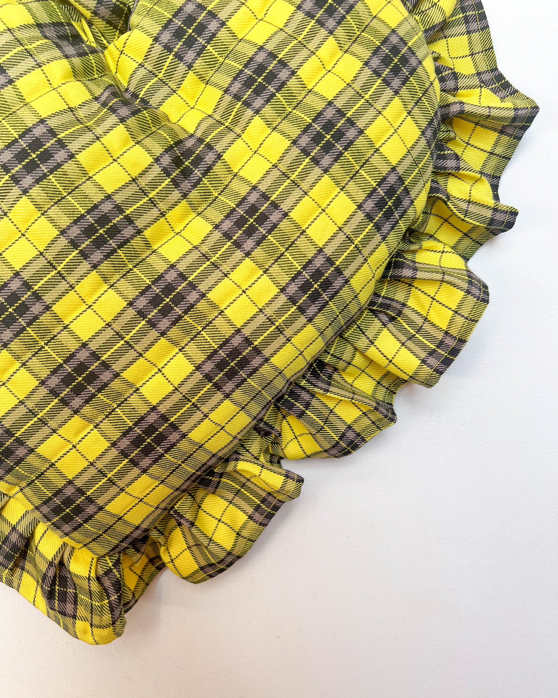 Yellow and black plaid fabric with ruffled edges on a white background